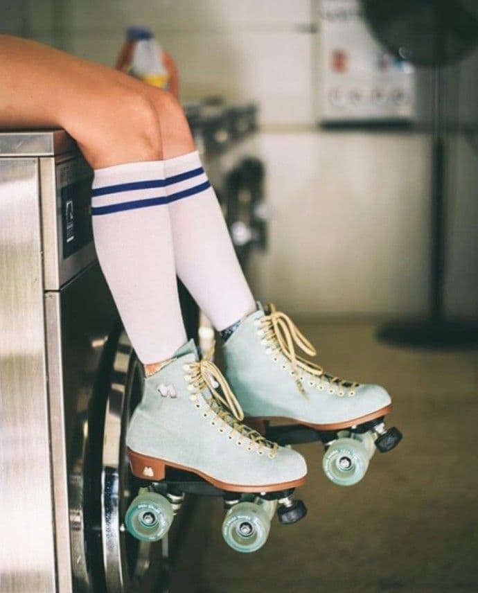 A pair of mint suede roller skates propped on top of a running washing machine in a laundromat.